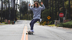 A man is swerving through a bare street on a longboard with his hands in the air. 