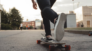 A person is pushing a longboard with their right foot on the board. Their left foot is hanging in the air behind the right leg.